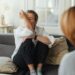 A woman wipes tears during a therapy session on a couch indoors.